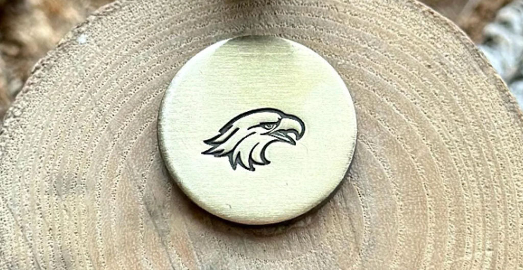 Macro du poinçon tête d'aigle gravé sur le fermoir d'une créole en or 18 carats, avec loupe d'orfèvre en arrière-plan d'atelier de joaillerie